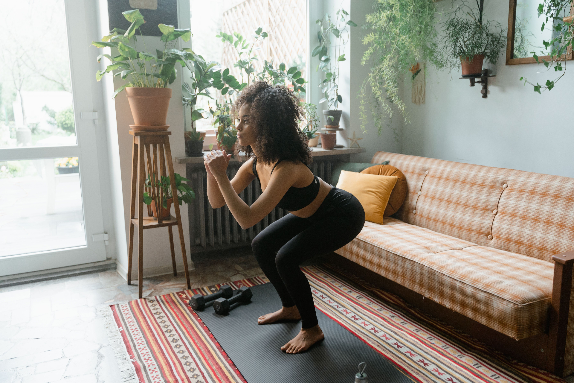 Woman doing a squat at home with dumbbells on a yoga mat